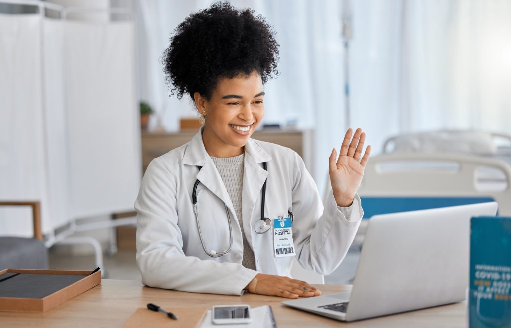 Young doctor waving to virtual care patient through laptop